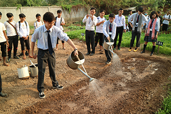 空芯菜の種植え体験授業で畑に水をまく日本高校生(学校訪問・授業体験)